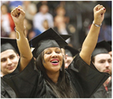 Female student celebrating with hands up in graduation gown