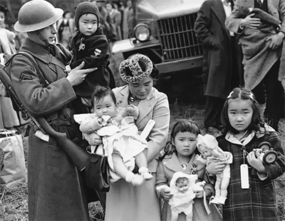 Cpl. George Bushy, left, holds the youngest child of Shigeho Kitamoto, center, as she and her children are forced to leave Bainbridge Island, Wash., in 1942. They were sent to an internment camp. (AP) 