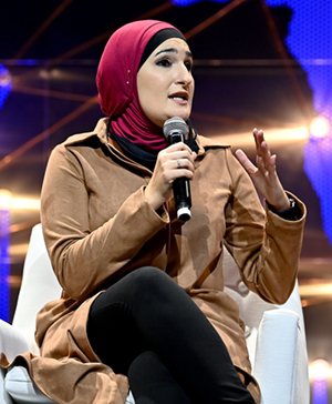 Linda Sarsour sitting in a chair with a mike on stage.