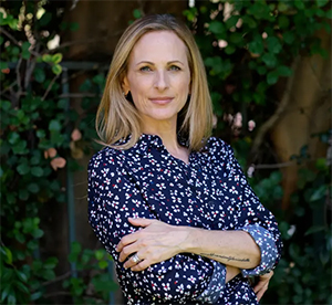 Marlee Matlin in flowered blue shirt with a green, tree background