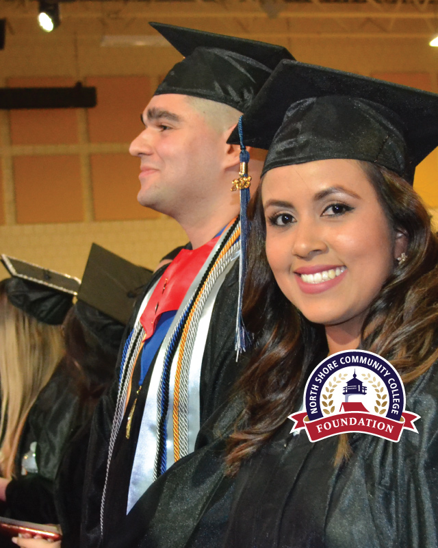 Smiling female graduating student at commencement with a smiling male graduate behind her.