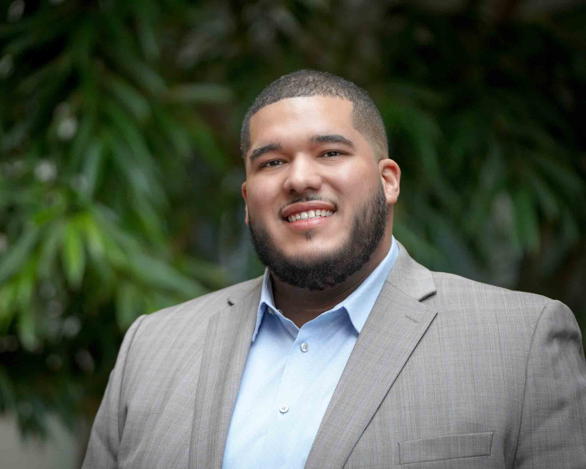 A man in a gray suit with a close cropped beard and short hair smiles at the camera
