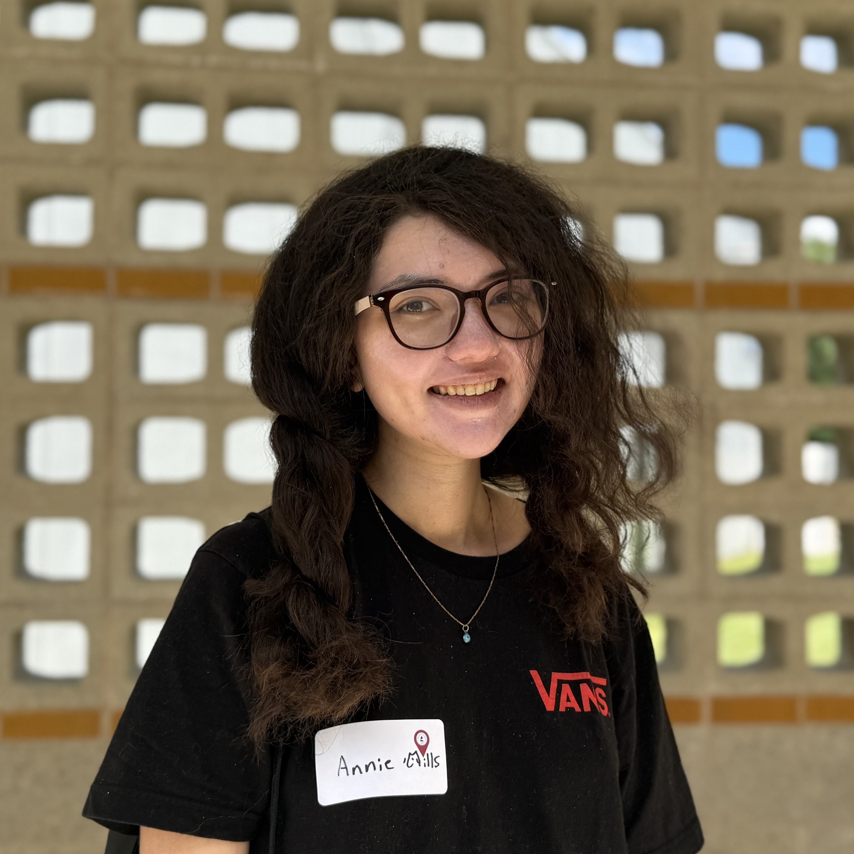 A person wearing glasses and a black t-shirt smiles at the camera