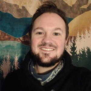 Portrait of Michael Jacob standing in front of a mountain painting 