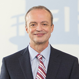 Portrait of Bill in blue suit n front of NSCC logo wall